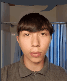 a young man in a gray shirt is standing in front of a shower curtain