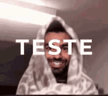 a man is wrapped in a blanket and smiling with the word teste written above him .