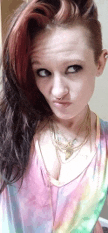 a woman with long hair and a nose ring is wearing a tie dye shirt and making a funny face .
