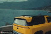 a yellow car is driving down a road near the ocean