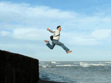 a man in a white shirt is jumping in the air over the ocean