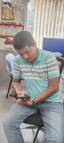 a man in a striped shirt sits in a chair looking at his phone