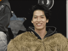 a young man wearing a fur coat is smiling