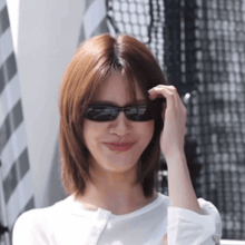 a woman wearing sunglasses and a white shirt smiles for the camera