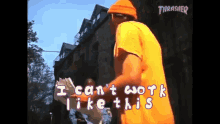 a man in an orange shirt is standing in front of a building with the words " i can 't work like this " written on it