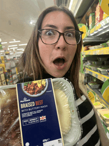 a woman in glasses holds a package of braised beef with buttery mash