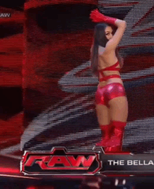 a woman in a red outfit is standing on a stage in front of a raw sign .