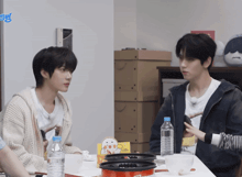 two young men are sitting at a table with a bottle of water and a box that says ' chicken ' on it
