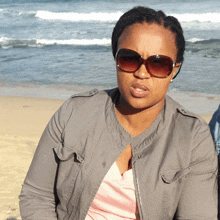 a woman wearing sunglasses and a grey jacket stands on the beach