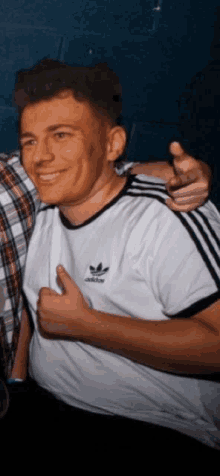 a man wearing a white adidas shirt is smiling and pointing at the camera