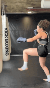 a woman in boxing gloves is kicking a kick boxing bag