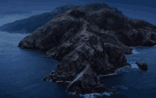 a dark cliff surrounded by water and mountains