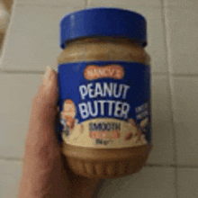 a person is holding a jar of nancy 's peanut butter .