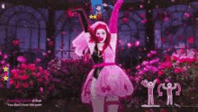 a woman in a pink dress and pink gloves is dancing in front of a bunch of flowers .