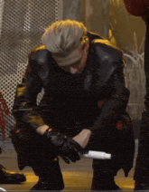 a man in a leather jacket and gloves is kneeling down on the floor holding a microphone .