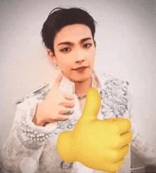 a young man is giving a thumbs up next to a yellow hand .