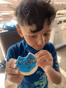 a young boy in a blue shirt is eating a cookie with blue frosting