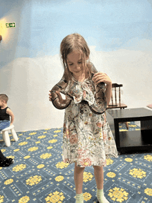 a little girl in a floral dress holds a large snake