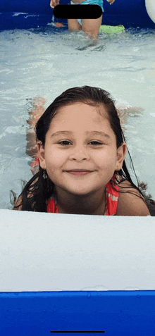 a little girl is laying in a pool and smiling for a photo