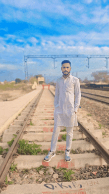 a man in a white kurta stands on the train tracks