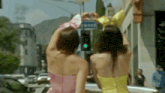 three women in pink and yellow dresses are standing in front of a green traffic light .