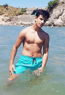 a shirtless young man in blue shorts is standing in the ocean .