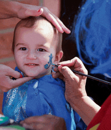 a baby is getting his face painted with a blue lizard