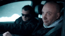 a bald man is sitting in a car next to another man