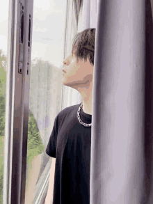 a young man in a black shirt is looking out of a window .