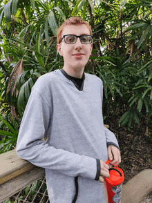 a young man wearing glasses and a grey sweater is holding a red container that says ' blood donation ' on it