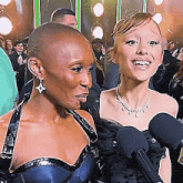two women are standing next to each other in front of microphones and smiling at the camera .