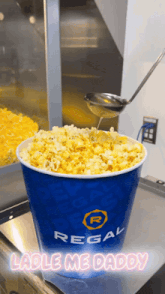 a bucket of regal popcorn is being poured with a spoon