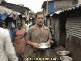 a man in a slum area is holding a bowl and says vote dedo bhiyoa