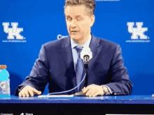 a man in a suit and tie stands in front of a microphone in front of a sign that says uk