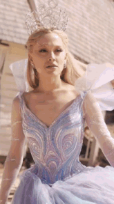 a woman in a blue dress with a crown on her head is standing in front of a building .