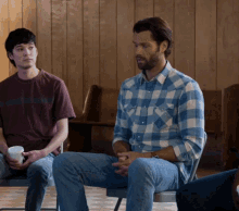 a man in a plaid shirt sits in a chair with other people