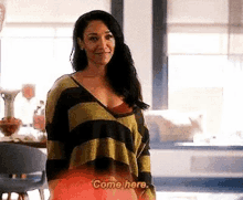 a woman in a striped sweater is standing in a living room and talking to someone .