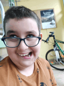 a boy wearing glasses and a brown shirt smiles in front of a sign that says sladom jesla