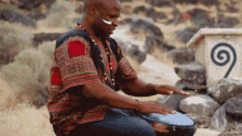 a man in a colorful shirt is playing a drum in front of a stone with a spiral on it