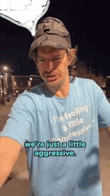 a man wearing a hat and a blue t-shirt is standing on a sidewalk at night .