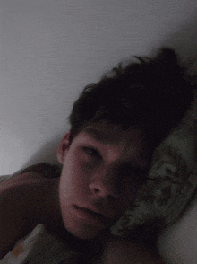 a young man laying in bed with his eyes closed and his head resting on a pillow