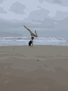 a girl is doing a handstand on a beach