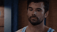 a man with a beard and a blue tank top looks down