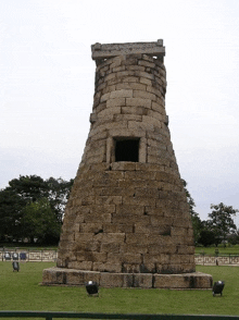 a large stone tower with a hole in the middle is surrounded by grass and trees .