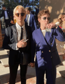 a man in a suit holds a glass of whiskey next to a woman in sunglasses