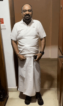 a man wearing a white shirt and a white skirt is standing in a hallway