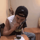 a man wearing a black hat with the letter t on it drinks from a glass