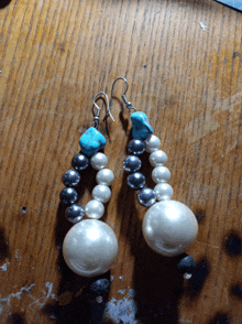 a pair of earrings with pearls and turquoise beads on a wooden table