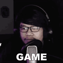 a man wearing headphones and glasses is talking into a microphone with the word game written on it .