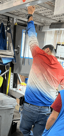 a man in a red white and blue shirt is reaching up to a shelf